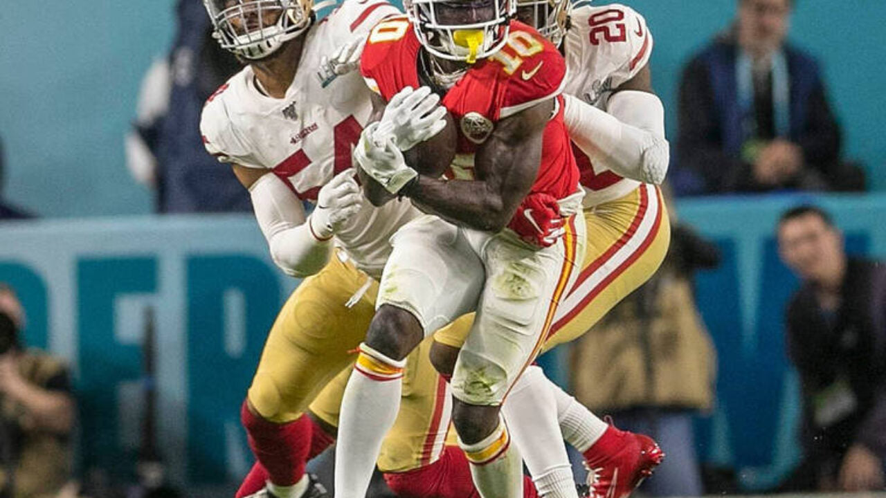 A football player mid-action scoring a touchdown in a stadium filled with cheering fans.